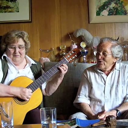 older German couple sitting on couch playing guitar and singing